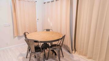 A room with a round wooden table and four chairs, beige curtains, and a light-colored floor.