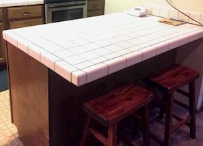 A kitchen with a tiled countertop, wooden stools, and a built-in oven.