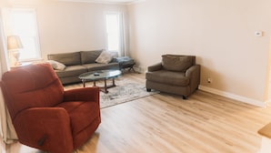 A living room with a red armchair, a brown sofa, and a glass coffee table. - Walk to Pro Football Hall of Fame! 5 Bedroom (Canton)