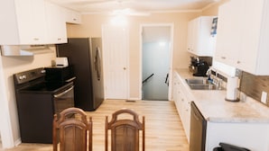 A kitchen with white cabinets, a black refrigerator, a stove, and a dishwasher. There is a dining table with chairs and a ceiling fan. - Walk to Pro Football Hall of Fame! 5 Bedroom (Canton)