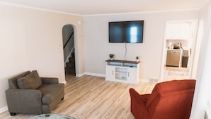 A living room with a sofa, a red armchair, a glass coffee table, and a flat-screen TV mounted on the wall. - Walk to Pro Football Hall of Fame! 5 Bedroom (Canton)