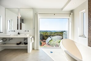 A modern bathroom with a large window, a bathtub, and a vanity with two sinks. - Vila Dria: modern luxury in the best part of the Algarve (Silves)