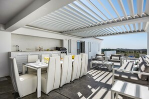 A modern outdoor dining area with a white table and chairs, a grill, and a view of the landscape. - Vila Dria: modern luxury in the best part of the Algarve (Silves)