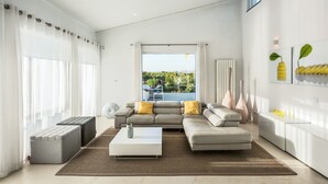 A modern living room with a sectional sofa, ottomans, a coffee table, and a view of the outdoors. - Vila Dria: modern luxury in the best part of the Algarve (Silves)