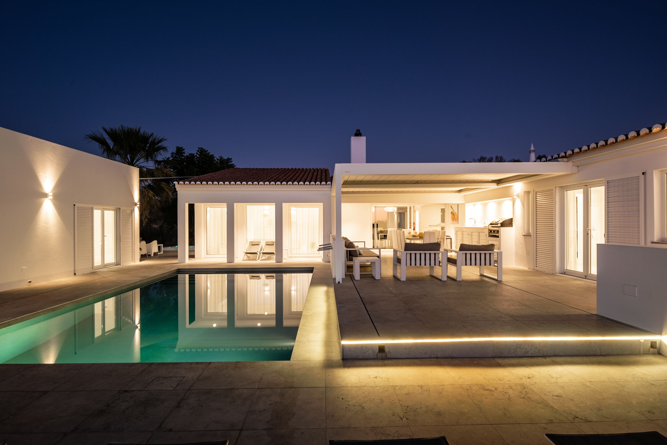 A modern house with a swimming pool, outdoor seating, and a well-lit patio area.