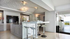 A modern kitchen with a large island, bar stools, and a view of the outdoors. - Vila Dria: modern luxury in the best part of the Algarve (Silves)