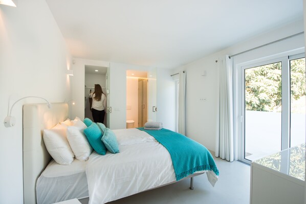 Un dormitorio moderno con una cama grande, vistas al exterior y un baño visible a través de una puerta abierta.