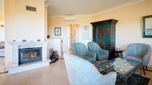 Un salon avec une cheminée, deux fauteuils, une table basse en verre et un meuble décoratif.
