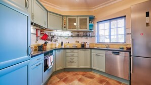 A kitchen with light blue cabinets, a stainless steel dishwasher, and a window with blinds.