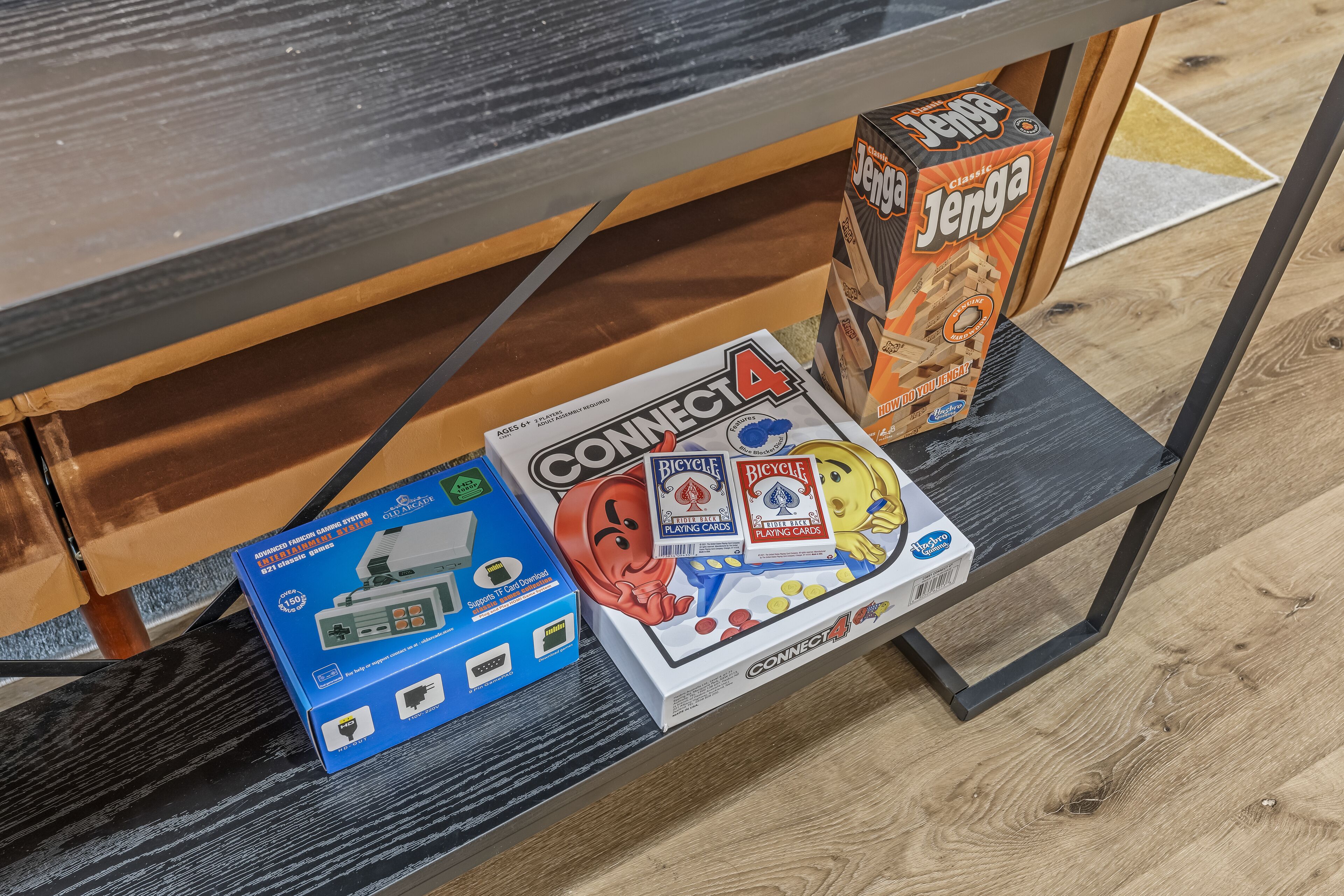 A wooden table with a black tabletop and a shelf underneath. On the shelf, there are several game boxes including Connect4, Bicycle, and Jenga.