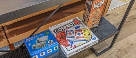A wooden table with a black tabletop and a shelf underneath. On the shelf, there are several game boxes including Connect4, Bicycle, and Jenga.