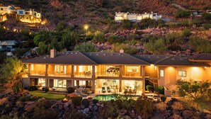 A large, multi-story house with a pool, surrounded by a landscaped garden and rocky terrain. - Camelback Heights - 8BR Estate w/ Pool, Theater & Camelback Views (Phoenix)