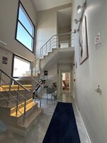 A modern interior with a staircase leading to a second floor, a desk with a chair, and a blue carpet.