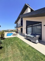 A modern two-story house with a swimming pool, outdoor furniture, and a view of the landscape.