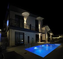 A modern two-story house with a swimming pool, outdoor furniture, and a balcony.