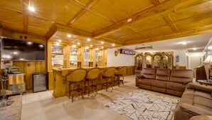Ein gemütliches Interieur mit Holzbalkendecke, einer Bar mit Hockern, einem großen braunen Sofa und einem gemusterten Teppich.