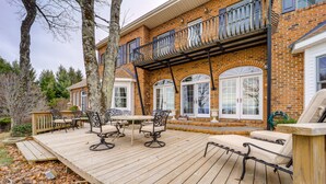 Eine Holzterrasse mit Gartenmöbeln, ein Ziegelhaus mit Balkon und ein großes Fenster.