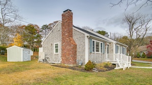 A single-story house with a brick chimney, a small porch, and a shed in the yard. - Rail Trail Access: Home 2 Mi to Lighthouse Beach! (Chatham)