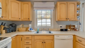 A kitchen with wooden cabinets, a dishwasher, a window with a view, and various kitchen appliances. - Rail Trail Access: Home 2 Mi to Lighthouse Beach! (Chatham)