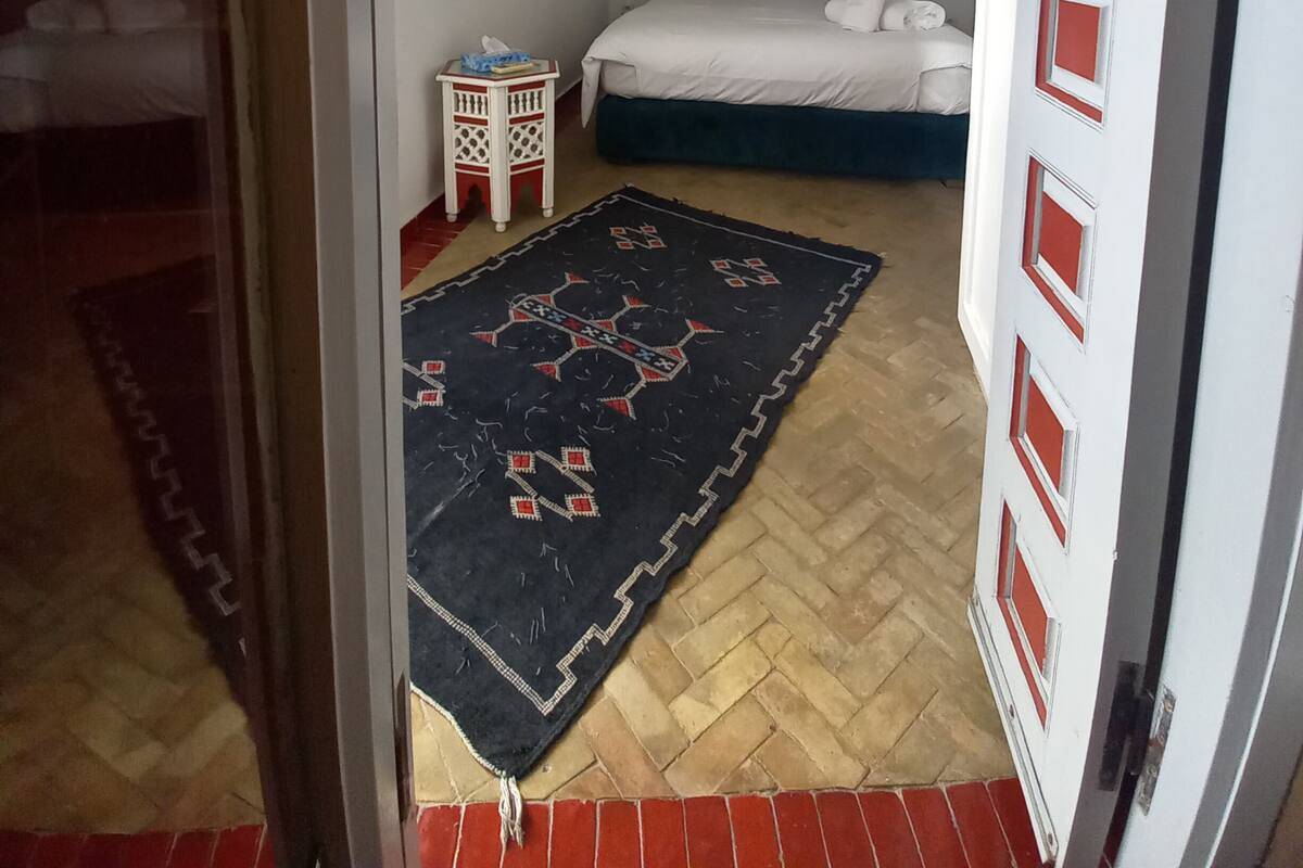 Une chambre à coucher avec un lit, une table de chevet, un tapis et une porte agrémentée de touches de couleur rouge.