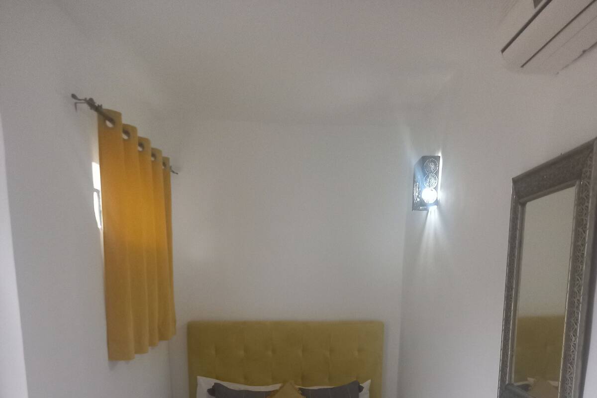 Un lit avec une tête de lit, une table de chevet, un miroir et une fenêtre avec des rideaux.
