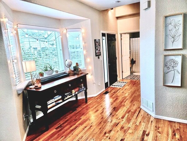A modern interior with a wooden floor, a black console table with decorative items, and framed artwork on the wall.