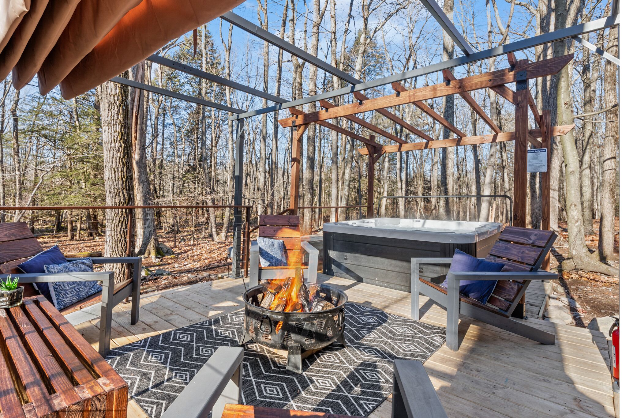Una terraza con una fogata, asientos y un jacuzzi en un área boscosa.