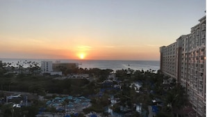 Ein Resort mit Poolbereich, Palmen und Blick auf den Sonnenuntergang über dem Meer.