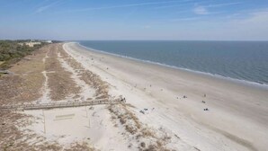 Une plage avec une longue étendue de sable, quelques personnes et une promenade en bois menant à un bâtiment.