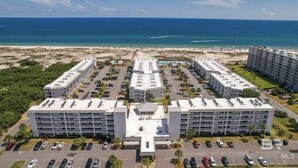 Ein mehrstöckiges Hotel mit Innenhof, Parkplätzen und Blick auf den Strand.
