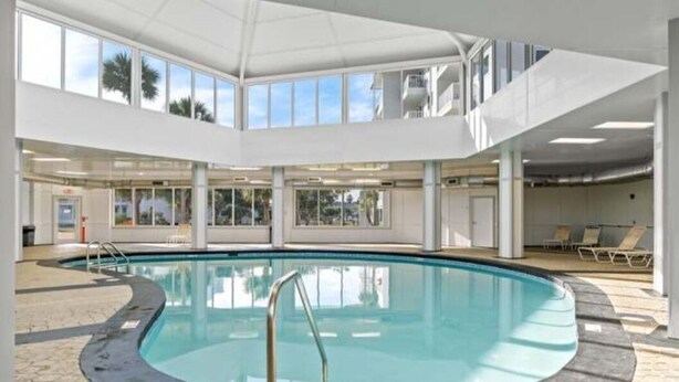 Ein Hallenbad mit freiem Blick zum Himmel durch große Fenster, umgeben von gefliestem Boden und einer weißen Deckenkonstruktion.
