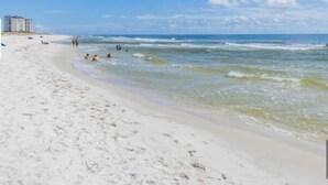 Ein Strand mit blauem Himmel, sandigem Ufer und ein paar Personen im Wasser.