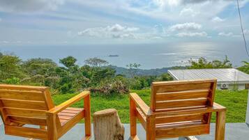 Two wooden chairs facing a scenic ocean view with a house in the background.