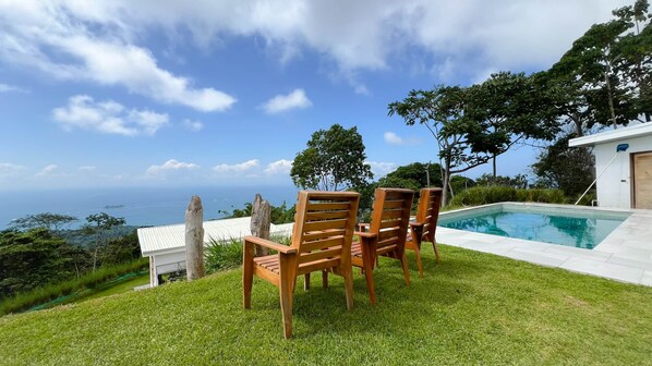 A pool with wooden chairs and a view of the ocean.