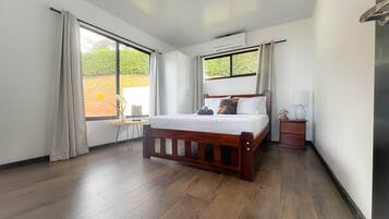 A bedroom with a wooden bed, a desk, and a window with curtains.