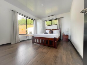 A bedroom with a wooden bed, a desk, and a window with curtains.