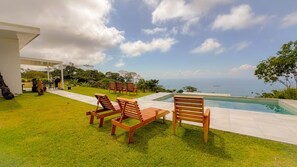 A poolside area with wooden loungers and a view of the ocean. - Panoramic Ocean Views & Private Pool | CARACARA 2bd (Uvita)