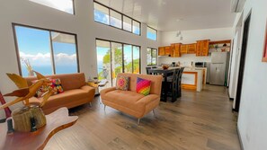 A spacious living area with a sofa and armchair, a dining table, and a kitchen with wooden cabinets. - Panoramic Ocean Views & Private Pool | CARACARA 2bd (Uvita)