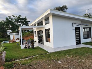 A modern two-story house with a covered patio, a swimming pool, and a well-maintained lawn. - Panoramic Ocean Views & Private Pool | CARACARA 2bd (Uvita)