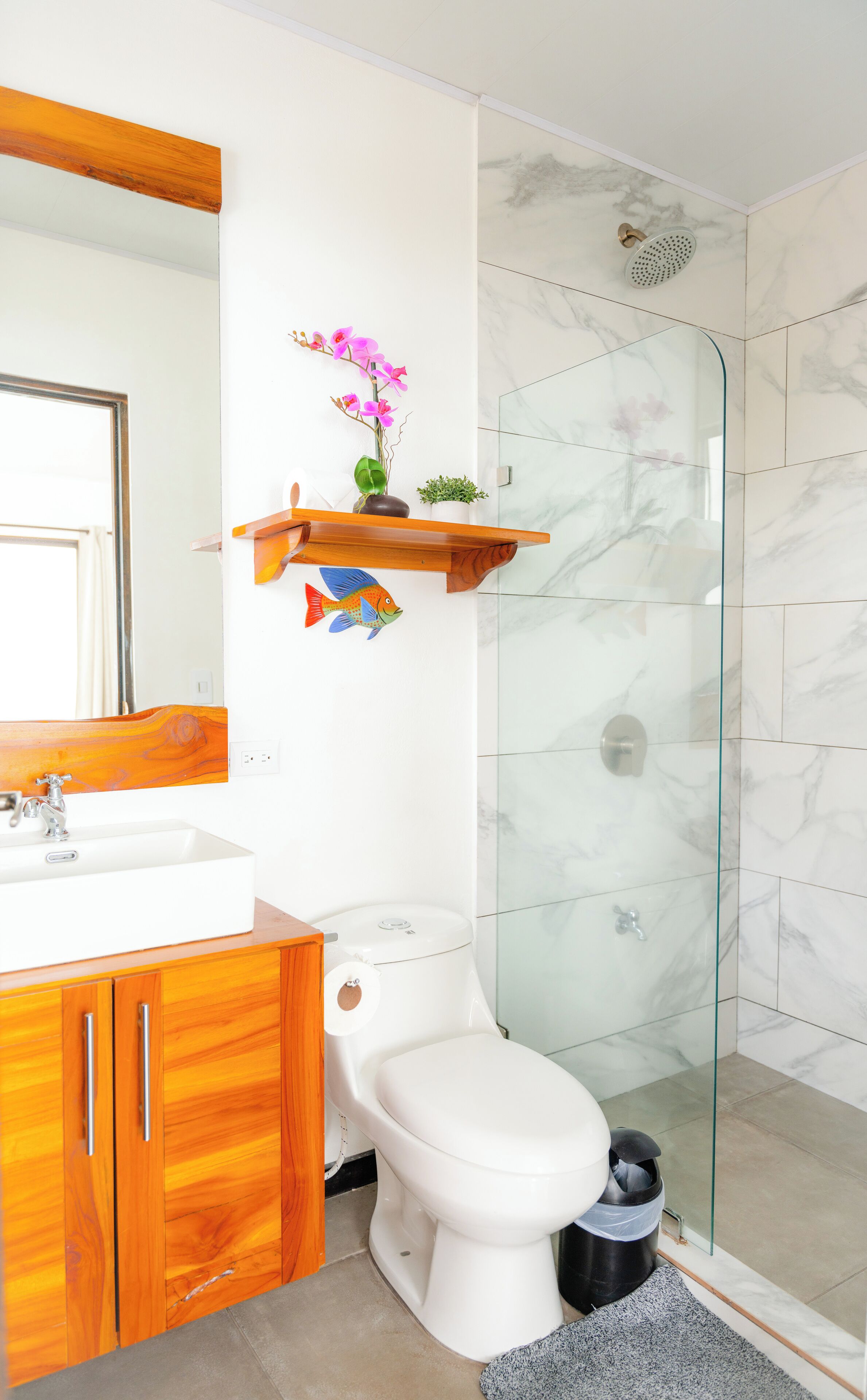A modern bathroom with a white toilet, wooden vanity, and a glass shower enclosure.
