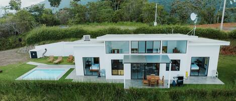Ein modernes, zweistöckiges Haus mit Swimmingpool, großen Fenstern und einer Terrassenanlage.