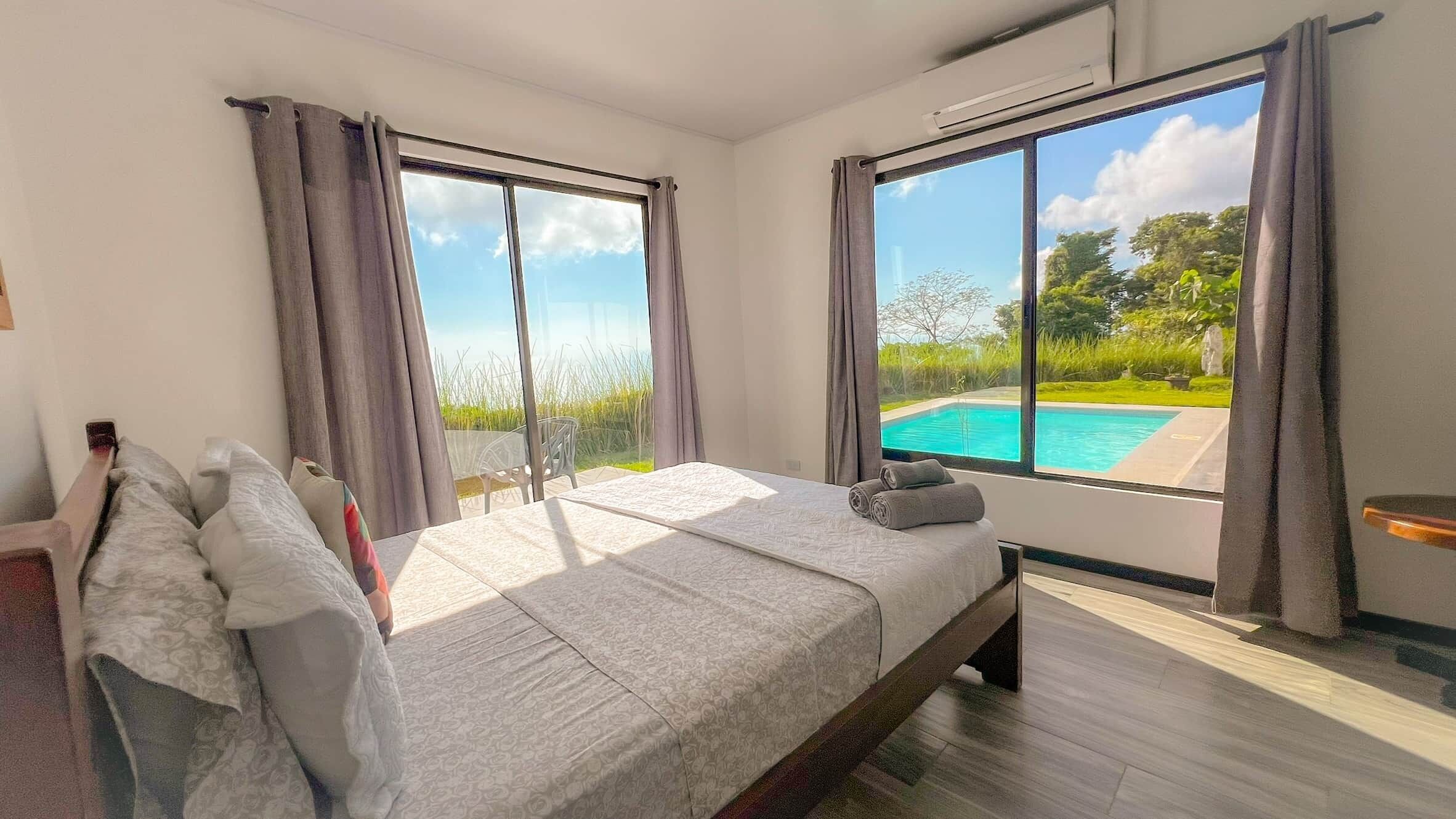 A bedroom with a large bed, a view of a swimming pool, and a balcony.