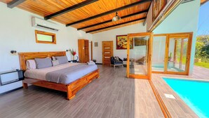 A bedroom with a wooden bed, a nightstand, a chair, and a glass door leading to a pool.