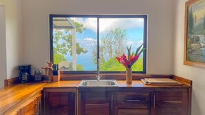 A kitchen with a large window, a sink, a coffee maker, and a vase with flowers. - 4bdr House in Uvita QUETZAL | Costa Rica (Uvita)