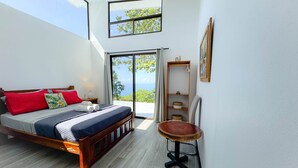 A bedroom with a bed, a small round table, a shelf, and a view of the outdoors. - 4bdr House in Uvita QUETZAL | Costa Rica (Uvita)