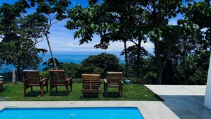 A pool area with four wooden chairs and a view of the ocean. - 4bdr House in Uvita QUETZAL | Costa Rica (Uvita)