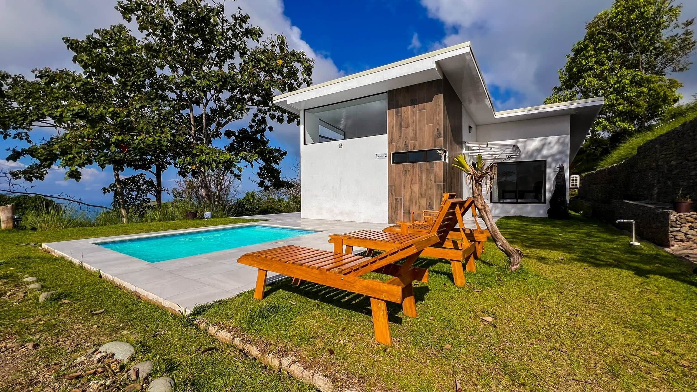 Ett modernt hus med en swimmingpool, träloungestolar och en stenmur.