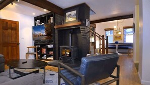 Una sala de estar acogedora con chimenea, televisión y una escalera que lleva a otra habitación.