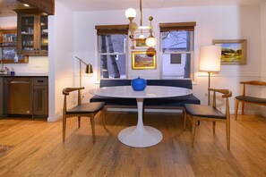 A dining area with a round table, four chairs, a blue vase, and a pendant light.