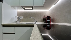 Una cocina moderna con un lavamanos de acero inoxidable, una cafetera y una placa de inducción roja.